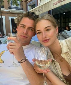 a man and woman pose for a photo while holding wine glasses in front of them