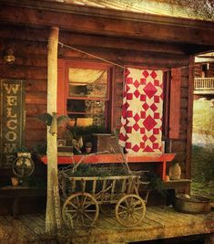 an old wooden house with a quilt hanging on the front door and a wheelbarrow