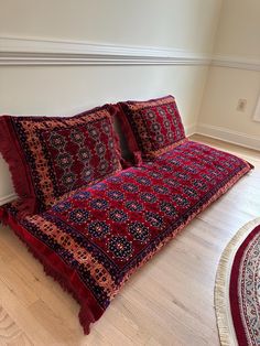 a bed with red and blue bedspread on top of it next to a rug