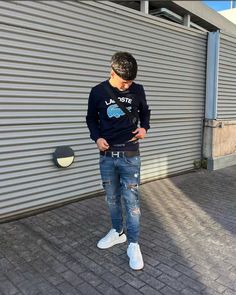 a young man standing in front of a garage door looking at his cell phone while wearing ripped jeans