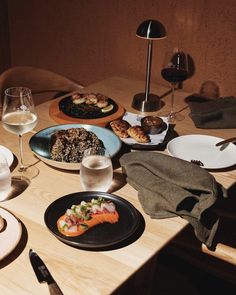 a wooden table topped with plates of food and glasses of wine on top of it