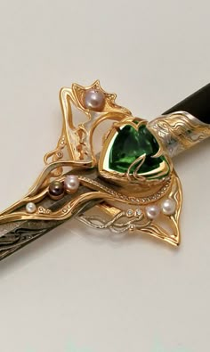 a green and gold brooch with pearls on it's side sitting on a white surface