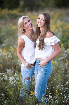 two beautiful young women standing next to each other in a field full of wildflowers