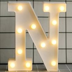 the letter n is lit up with light bulbs and sits in front of a tiled wall