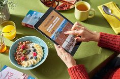 a woman is using her tablet to read the menu at a table with fruit and coffee