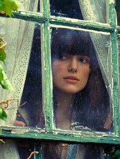 a woman looking out the window with her head in the window sill and curtain behind her