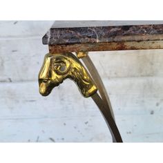 a brass horse head on a marble top table with a metal base and long curved legs