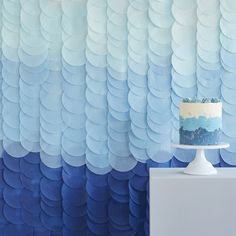 a blue and white cake sitting on top of a table next to a wall covered in wavy paper