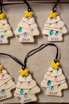 six ceramic christmas tree ornaments are hanging on a tray with black string and yellow stars