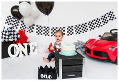 a baby boy sitting in front of a birthday cake with cars on the table next to it