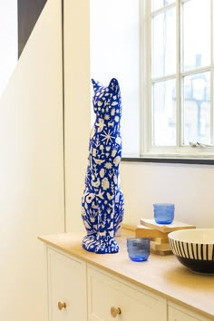 a blue and white cat statue sitting on top of a counter next to a bowl