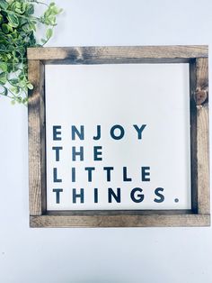 a wooden frame with the words enjoy the little things on it next to a potted plant