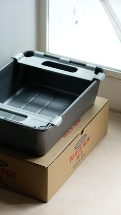 an empty box sitting on top of a cardboard box next to a window sill