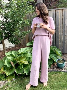 a woman standing in front of a garden holding a cup and looking at her cell phone