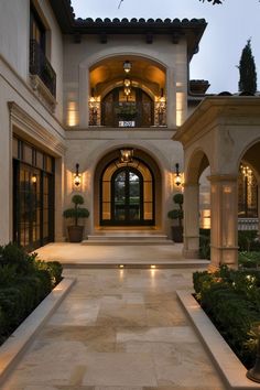 the entrance to a large house with lights on it's windows and plants in pots