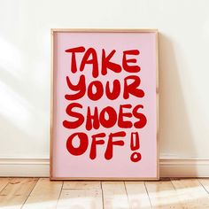 a pink poster with the words take your shoes off written in red on it, against a white wall