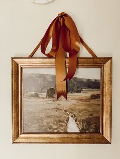 a painting hanging on the wall with a brown ribbon