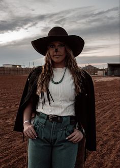 a woman with long hair wearing a cowboy hat and jeans in the middle of a field