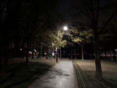 an empty path in the middle of a park at night with street lights shining on trees