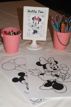 a table topped with two cups filled with markers and pencils next to a mickey mouse poster