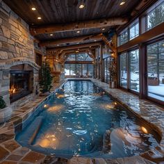 a large indoor swimming pool in the middle of a living room with stone fireplace and windows