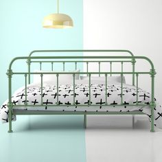 a green metal bed with white sheets and black crosses on the bedspread, next to a light blue wall