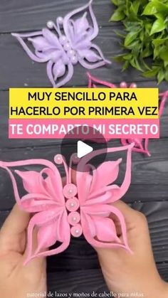 someone is holding some pink paper butterflies in front of a wooden table with green plants