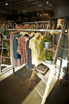 an old wooden ladder with clothes hanging on it in front of a rack full of shirts