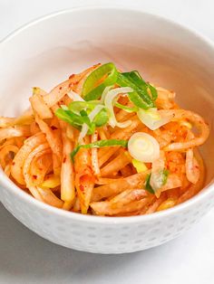 a white bowl filled with pasta and veggies on top of a marble table