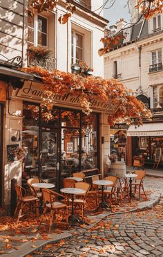 an outdoor cafe with autumn leaves on the ground and tables set up in front of it