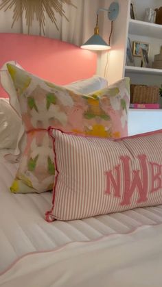 two pillows sitting on top of a bed with pink and white sheets in the background