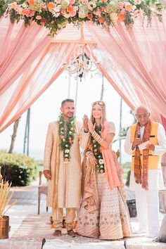 a man and woman standing under a pink canopy with flowers on it's head