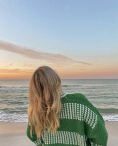 a woman standing on top of a sandy beach next to the ocean at sunset or dawn