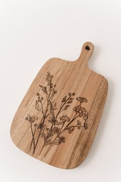 a wooden cutting board with flowers engraved on the front and sides, sitting on a white surface