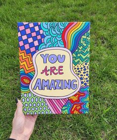 someone is holding up a book with the words you are amazing on it in front of some grass