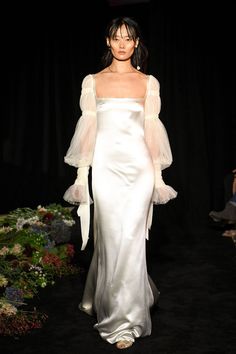 a woman walking down a runway in a white dress