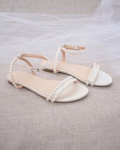 a pair of white shoes with pearls on the toes and straps, sitting on a bed