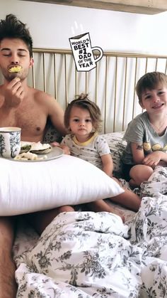 a man and two children sitting on a bed with food in front of their faces