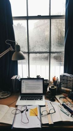 an open laptop computer sitting on top of a wooden desk next to a window filled with books