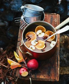 an apple cider with apples, oranges and cinnamon on a wooden table next to a metal pot