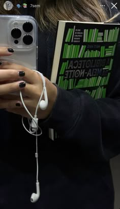 a woman with black and white nail polish holding a book while wearing headphones on her ear