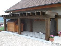 an outdoor dog house with a fence and flowers on the ground outside it, in front of a building