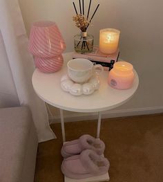 a white table topped with candles next to a pink vase filled with flowers and other items