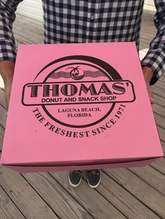 a man is holding a pink box that says thomas's donut and snack shop