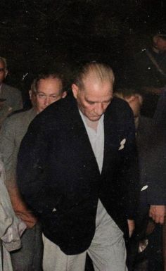 a man in a black jacket and white shirt is walking through a group of people