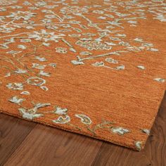 an orange rug with white and green flowers on it in a room that has wood floors