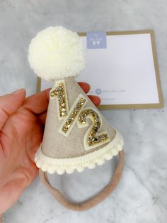 A handmade party hat perfect for marking 6 months of being born! Half birthday celebrations! A natural shade linen, with cream/off white wool pompom, pompom trim finished with gold glitter 1/2 (6 months). Other colours available at request (this listing is for the natural linen/gold glitter). Mini party hat measures 10cm high x 7cm at the base. Please note they are all made by hand so measurements may vary. The party hat is super soft and lightweight. It's made using premium fabrics including linen, wool and glitter fabric. The underside of the hat (the part of the hat that will sit on babies head) is lined with wool felt and the band to secure the hat on babies head is super soft and stretchy so it will be comfortable to wear. This party hat can be made using the other colours featured in 1/2 Birthday Hat, 6 Month Birthday, Wool Pompom, Flag Cake Topper, Cake Smash Photoshoot, Old Cake, Smash Photoshoot, Half Birthday, 2 Birthday