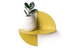 a white vase sitting on top of a yellow shelf next to a green leafy plant