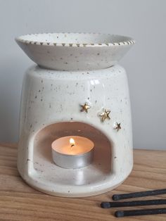 a white ceramic candle holder sitting on top of a wooden table next to two forks