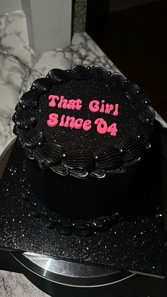 a black cake with pink writing on it sitting on top of a counter next to a knife